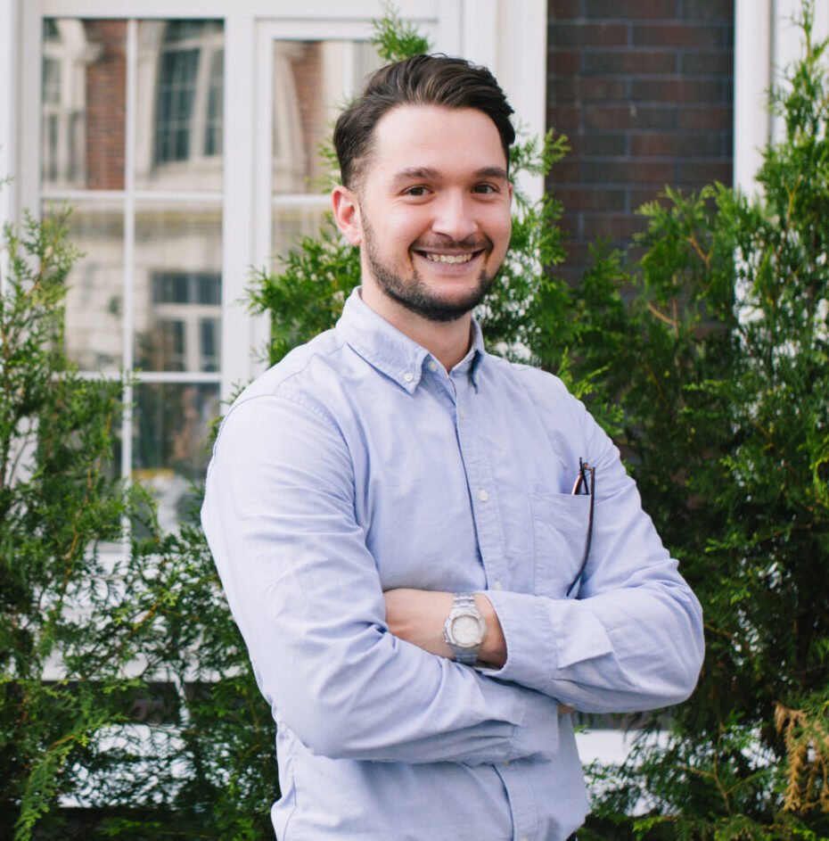 A smiling man with crossed arms in front of bushes | HOME SECURITY INSTALLATIONS.